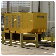 A large yellow metal standby generator on concrete outside of a building